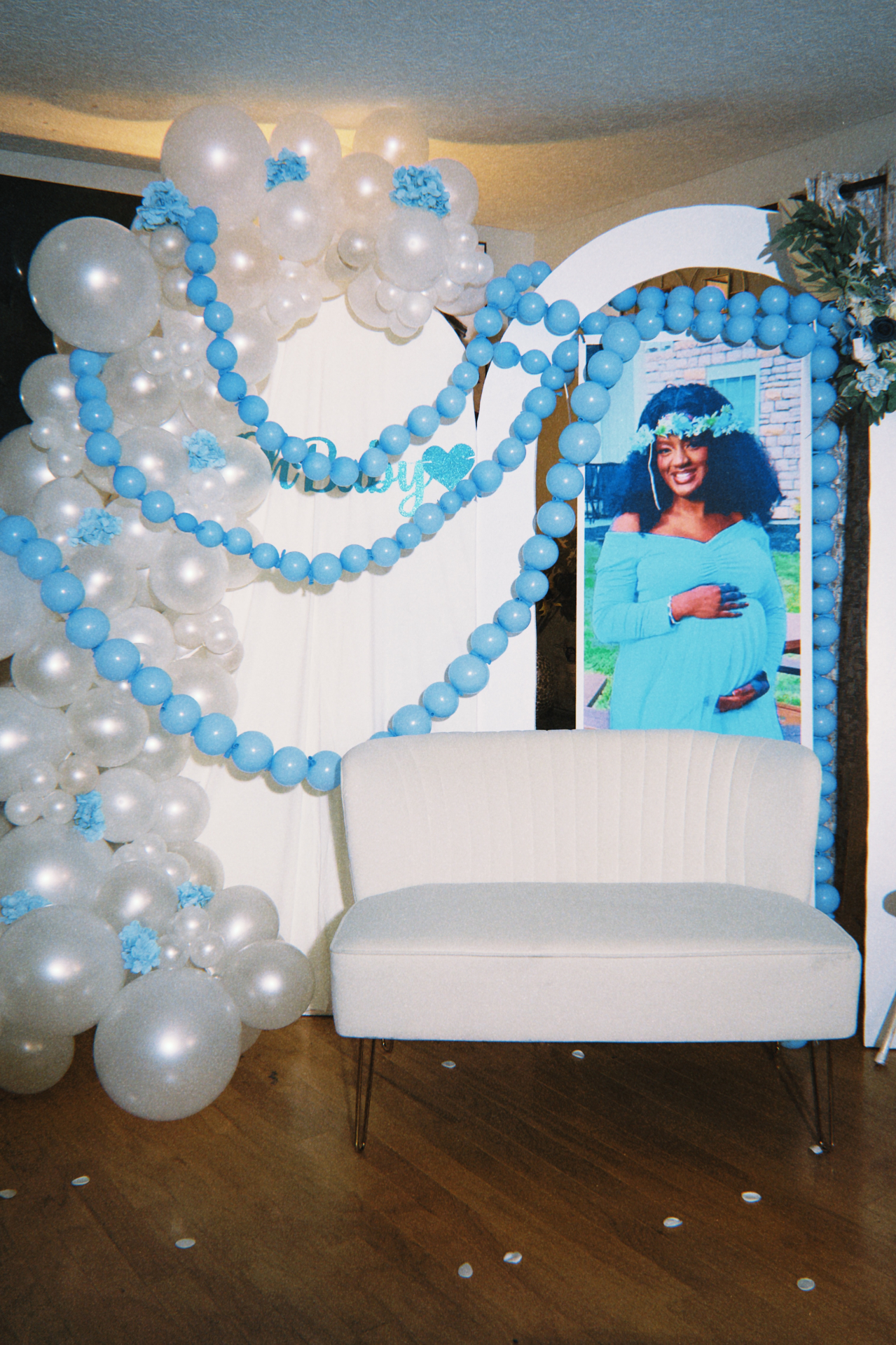 Blue and ivory baby shower setup with heart balloon garlands, portrait display, and ivory loveseat.