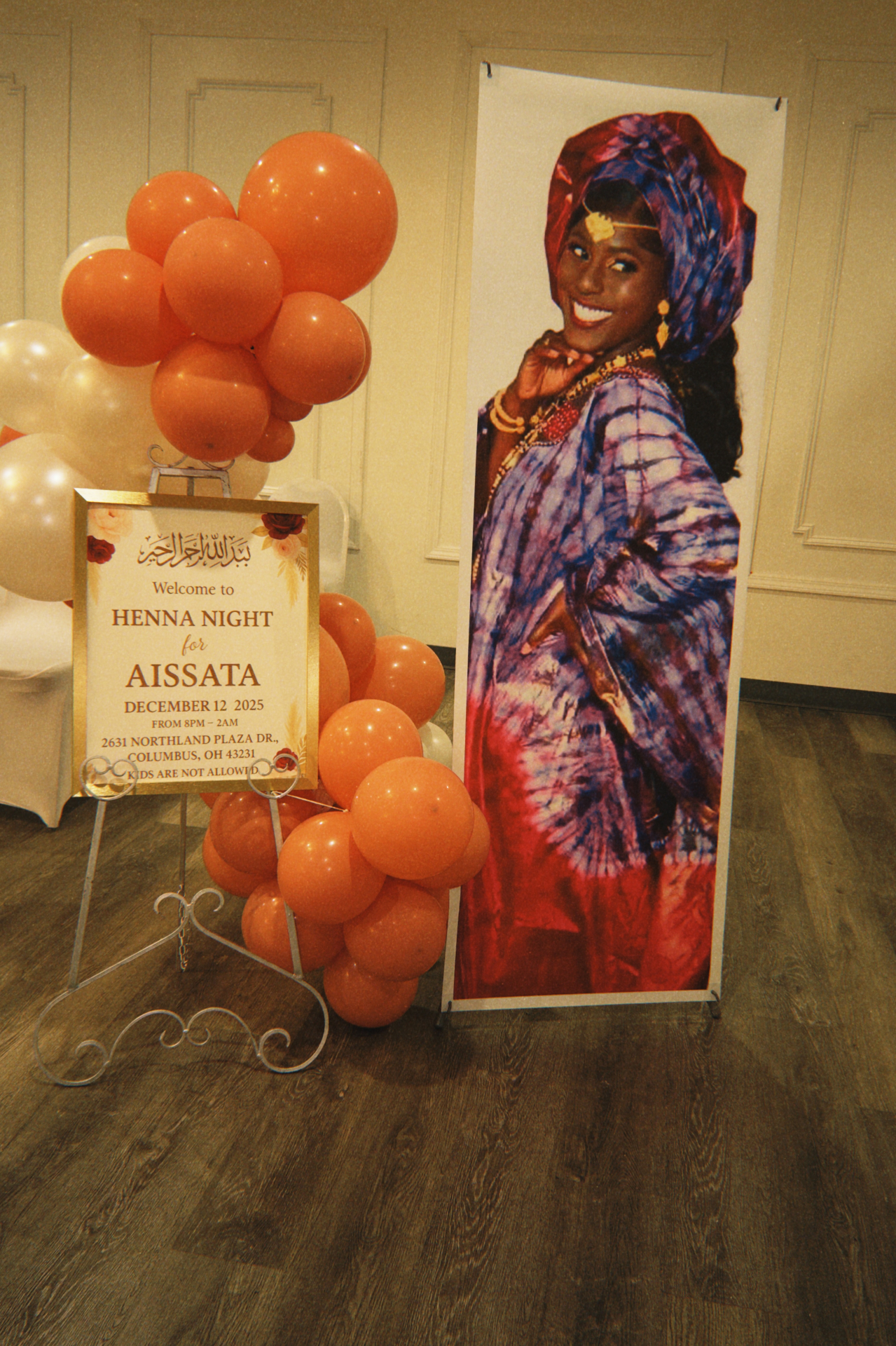 Henna Night entry moment with custom welcome sign, coral balloons, and portrait banner.